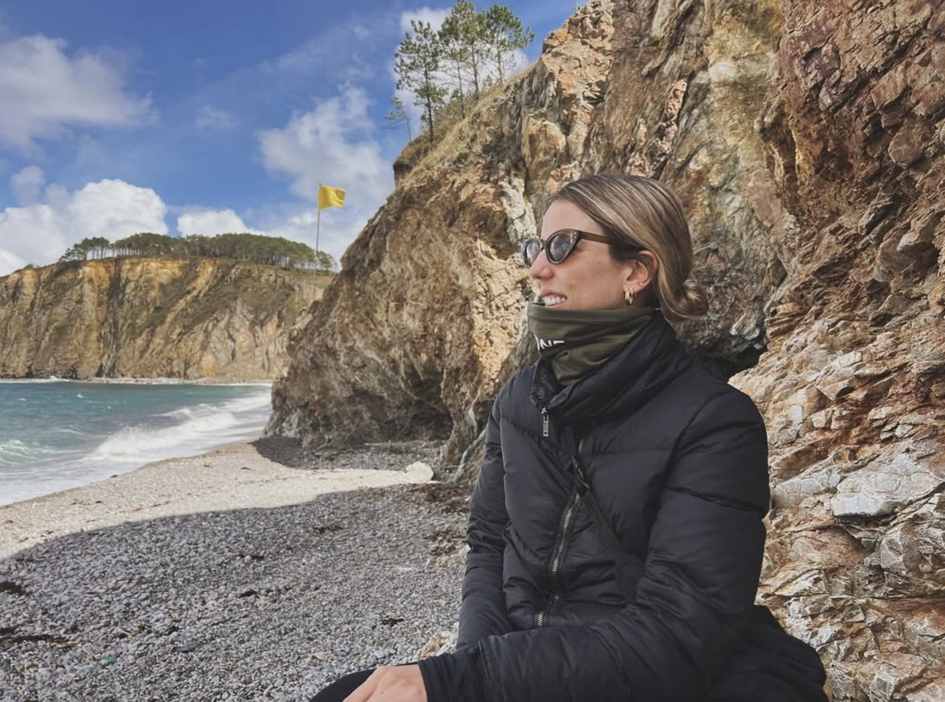 Woman sitting on a rocky beach with ocean and cliffs in the background